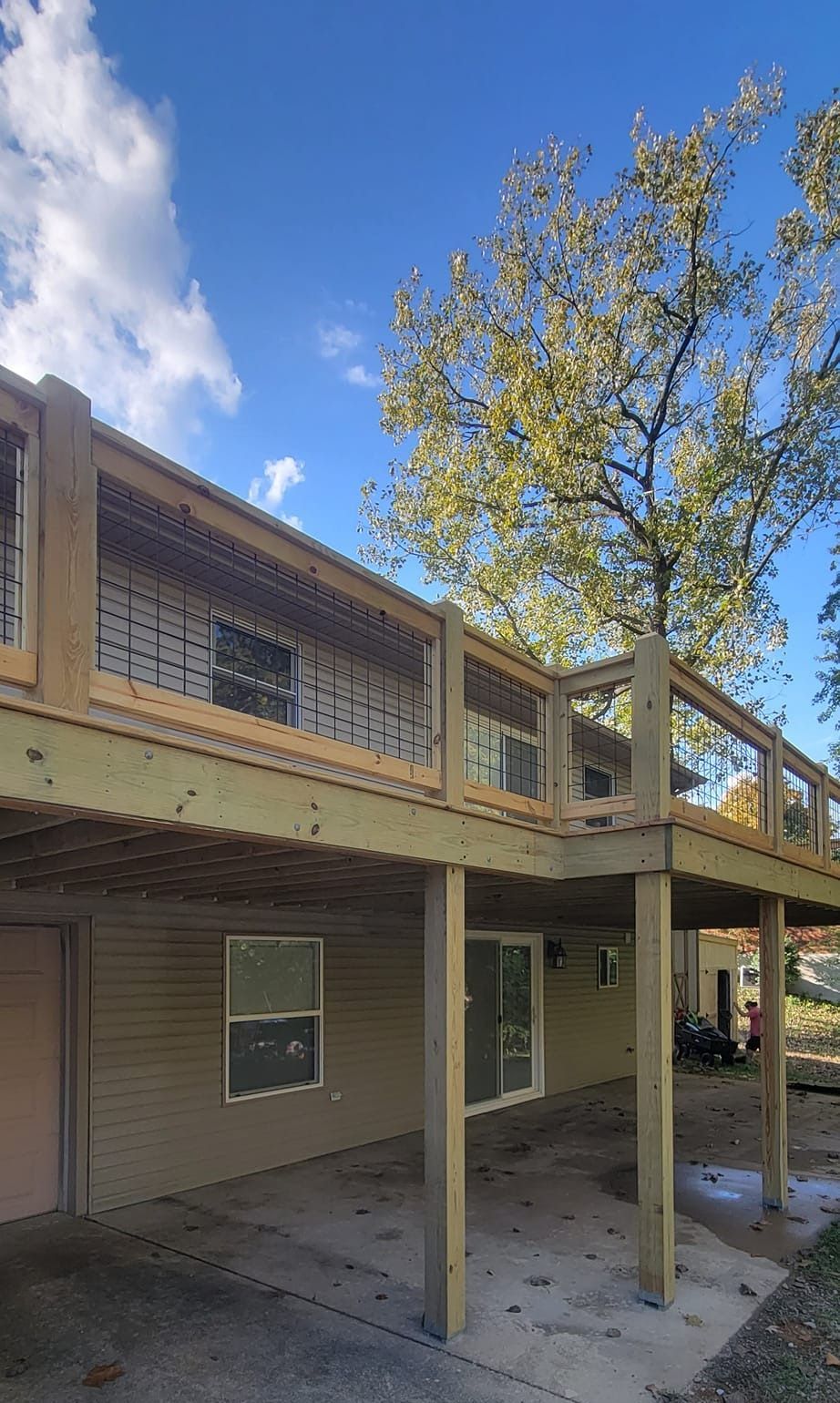 A house with a large deck and a tree in front of it.