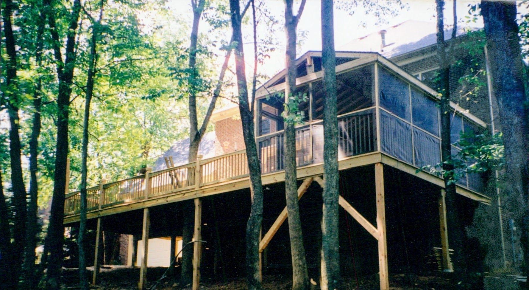A house with a large deck is surrounded by trees.