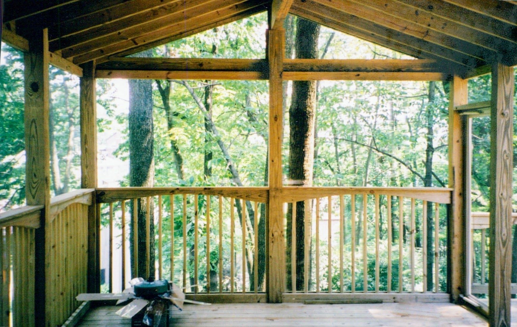 A screened in porch with a ceiling fan and a view of trees.