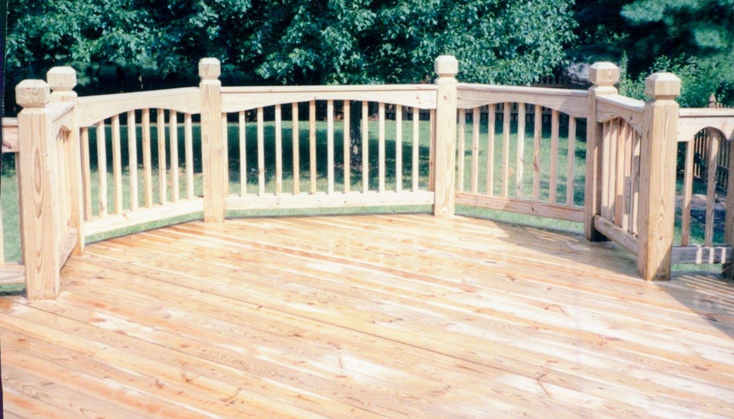 A wooden deck with a wooden railing and trees in the background.