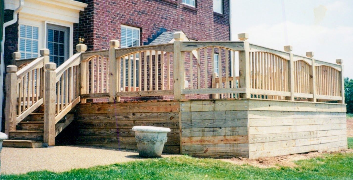 A wooden deck with stairs is in front of a brick house.