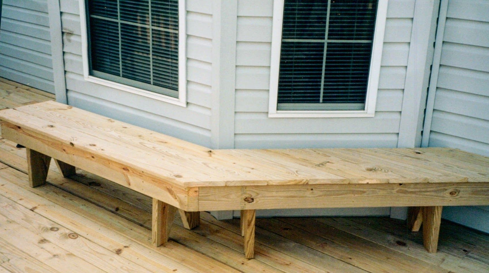 A wooden bench on a deck next to a window
