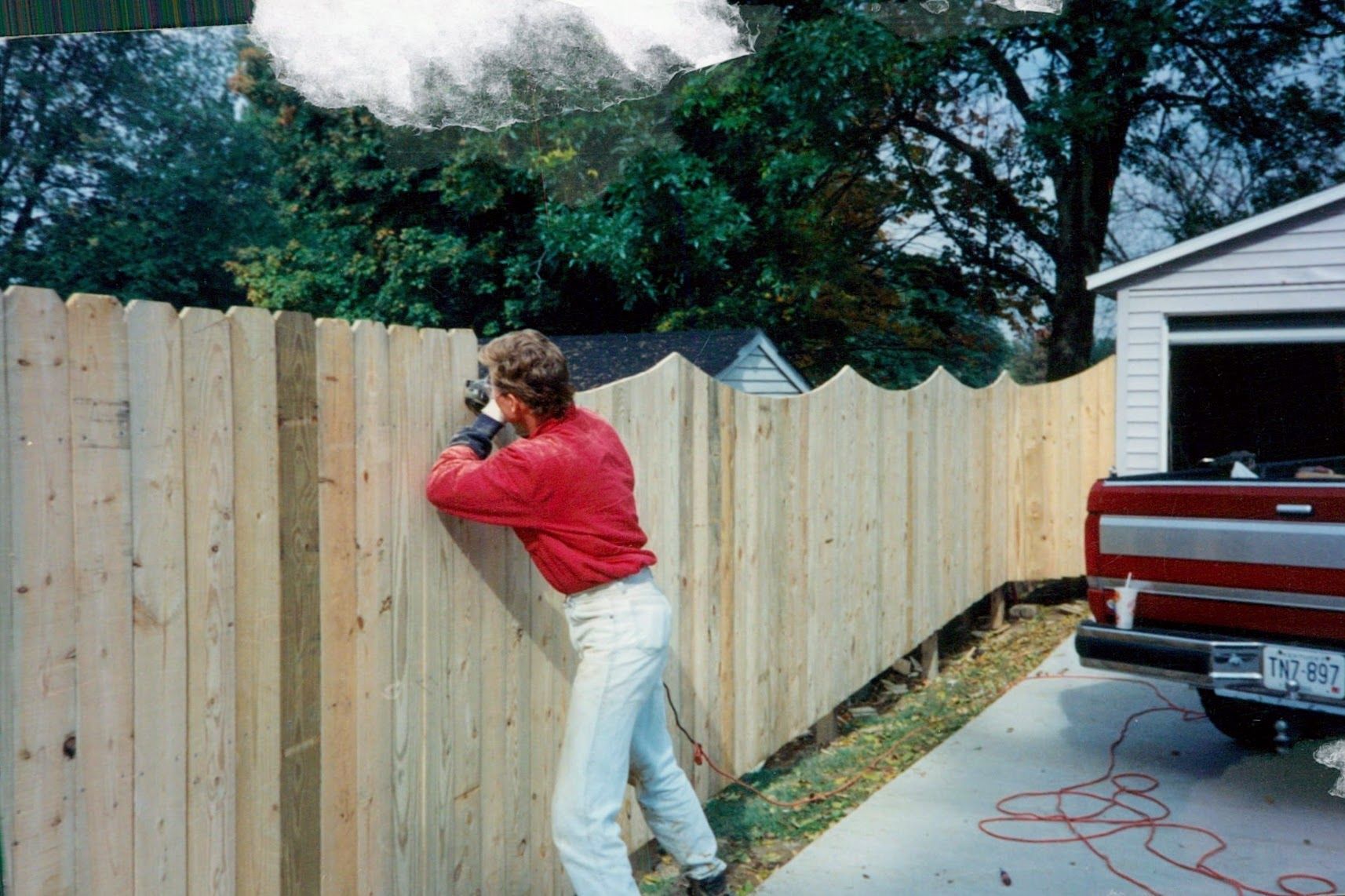 A man in a red shirt is working on a wooden fence