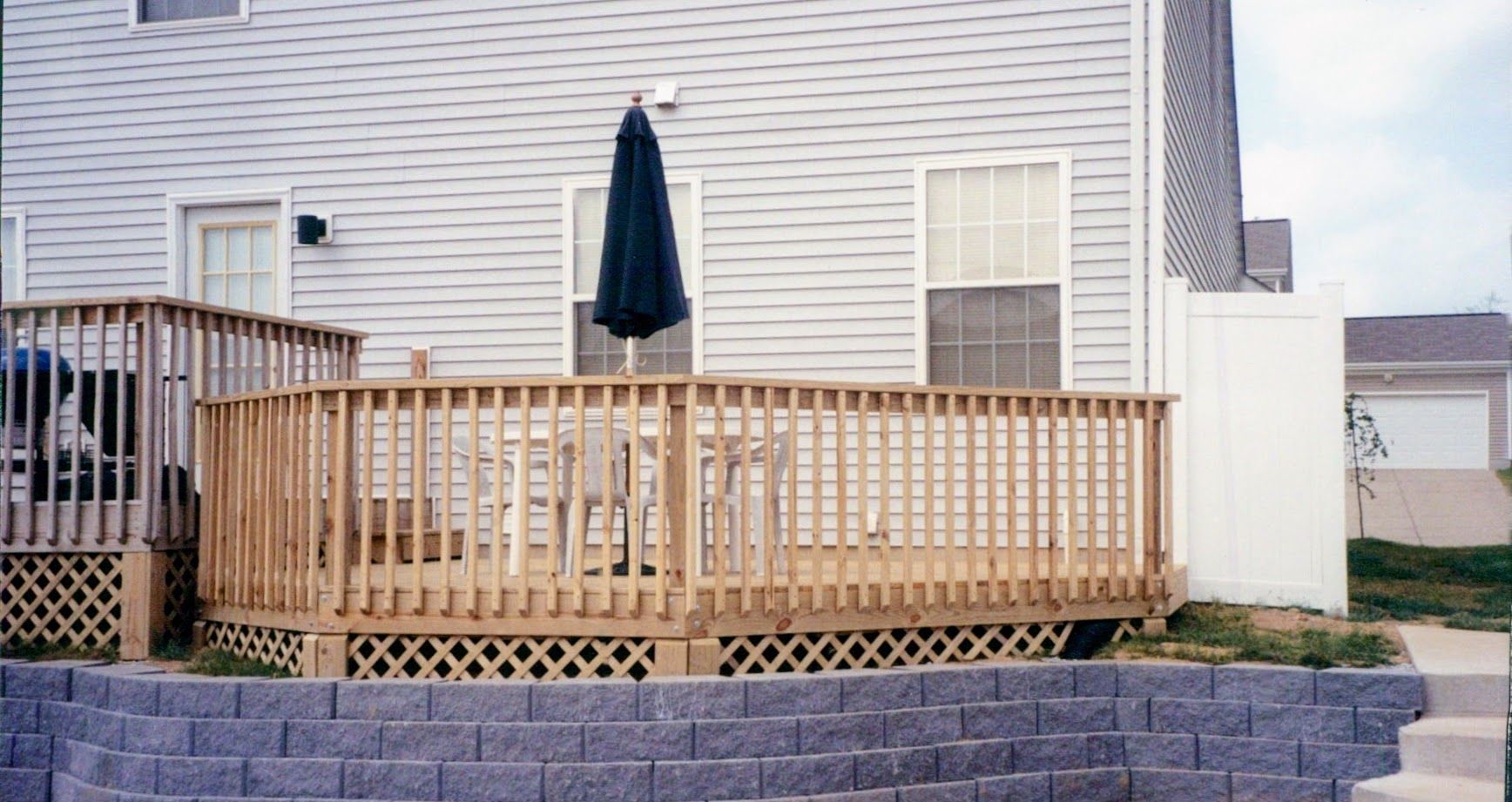 A white house with a wooden deck and a blue umbrella