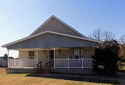 A brick house with a large porch and a white railing.