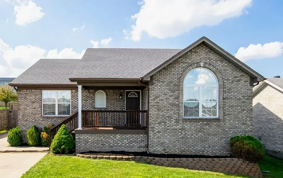 A small brick house with a gray roof and a large window.