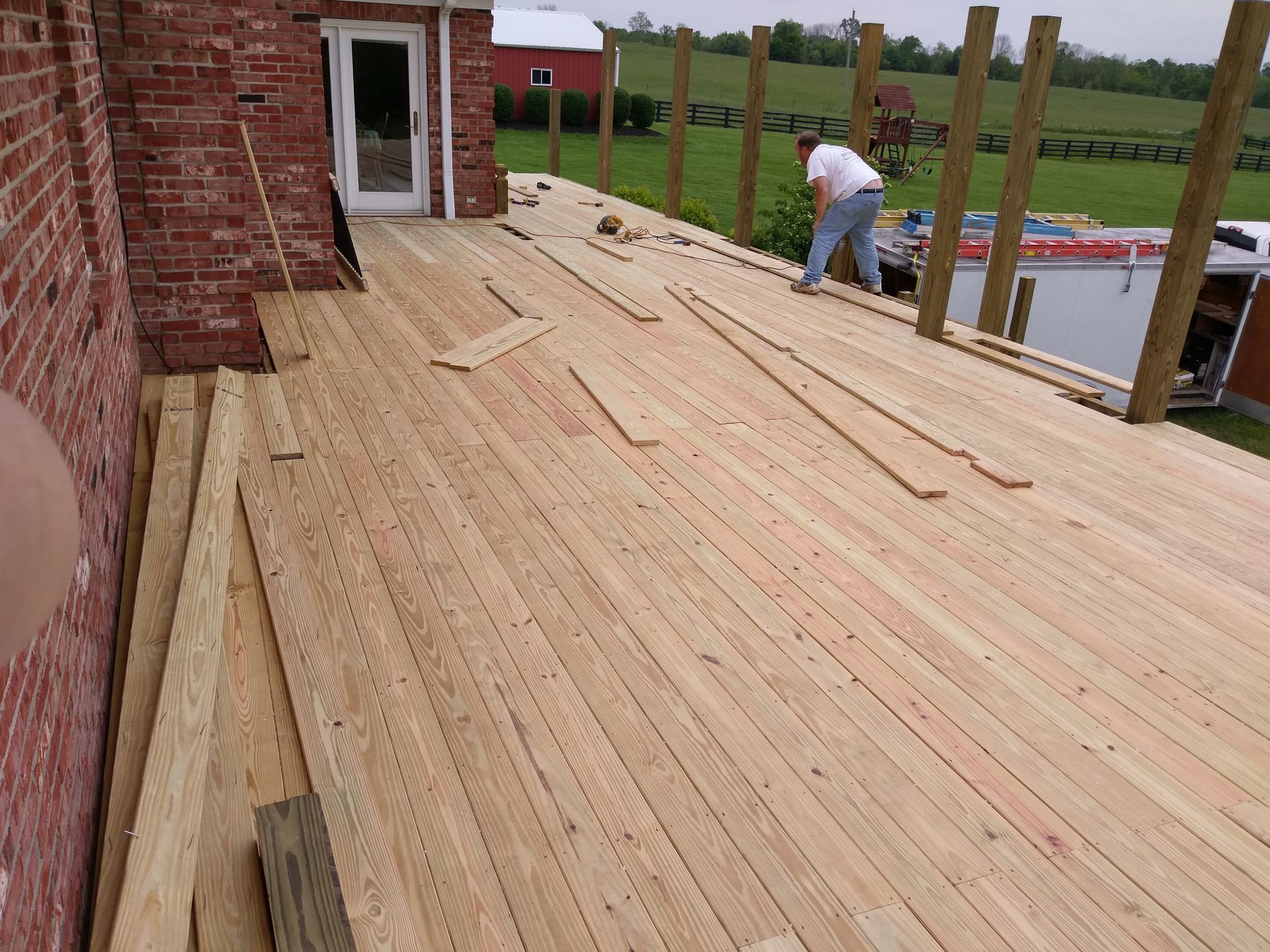 A man is working on a wooden deck in front of a brick building