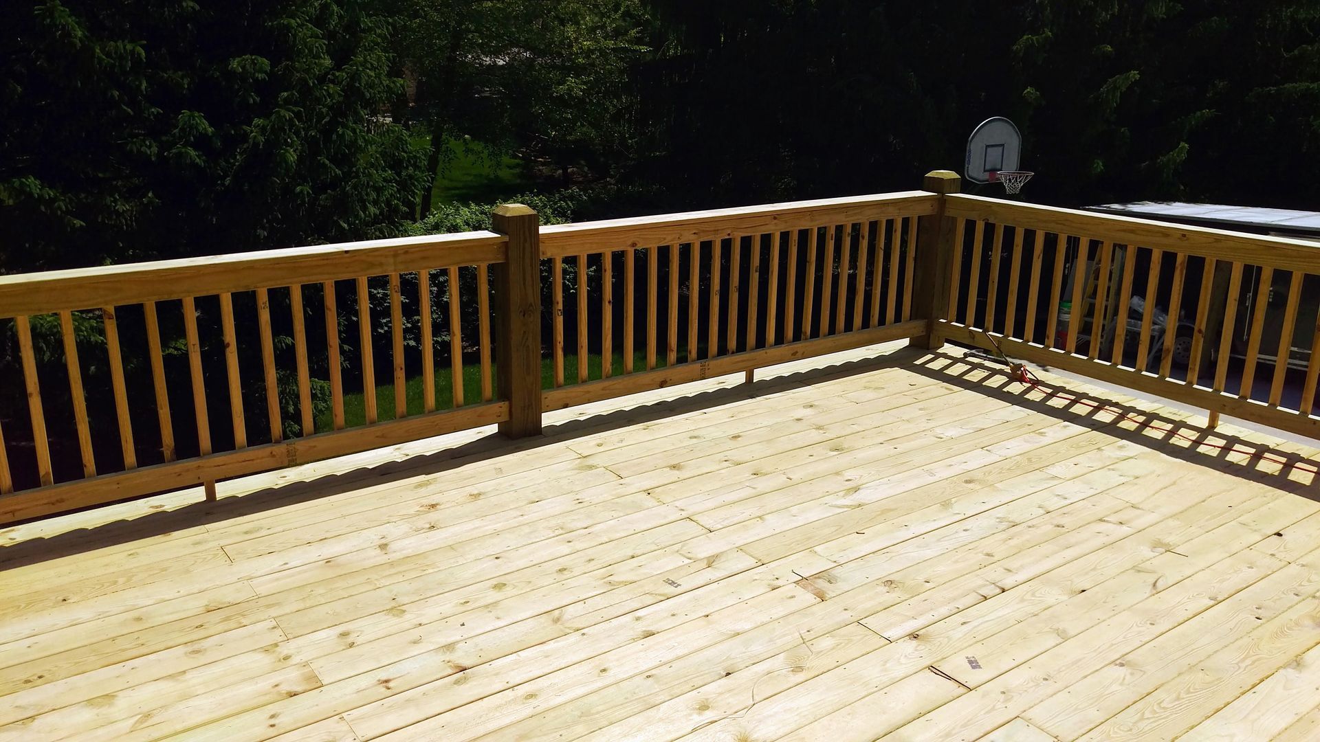 A wooden deck with a wooden railing and a basketball hoop in the background.