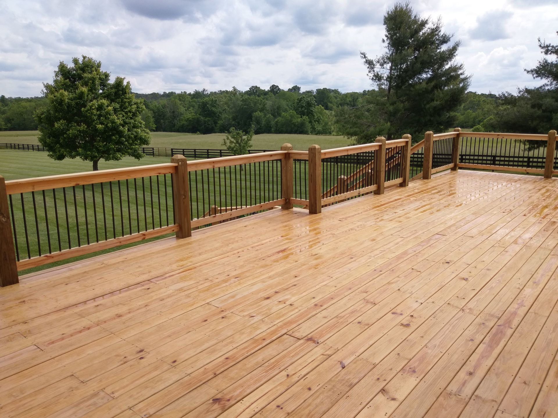 A large wooden deck with a metal railing overlooking a field