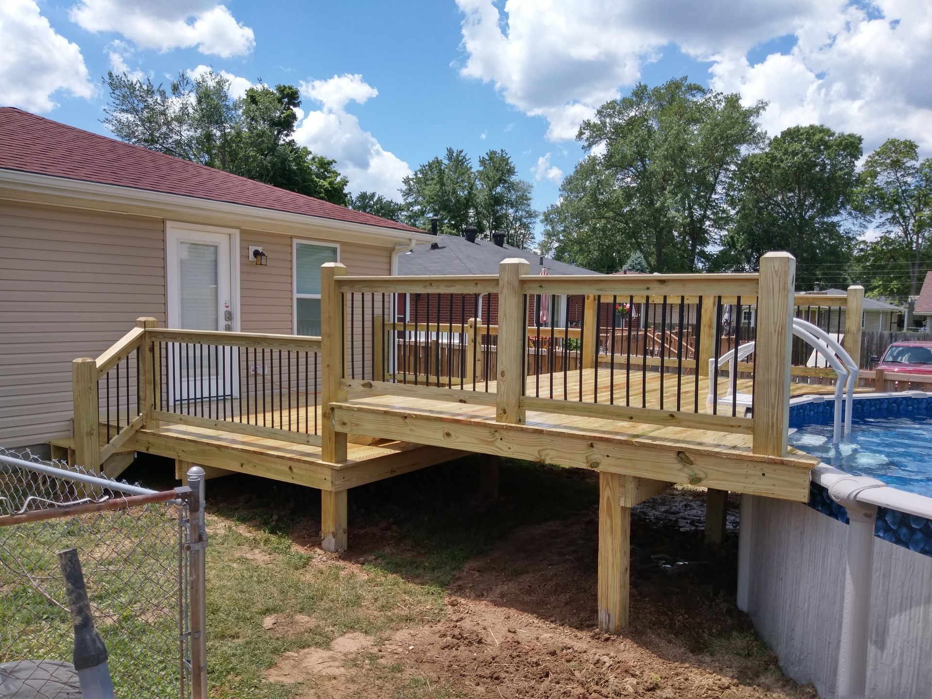 A wooden deck is sitting next to a pool in front of a house.