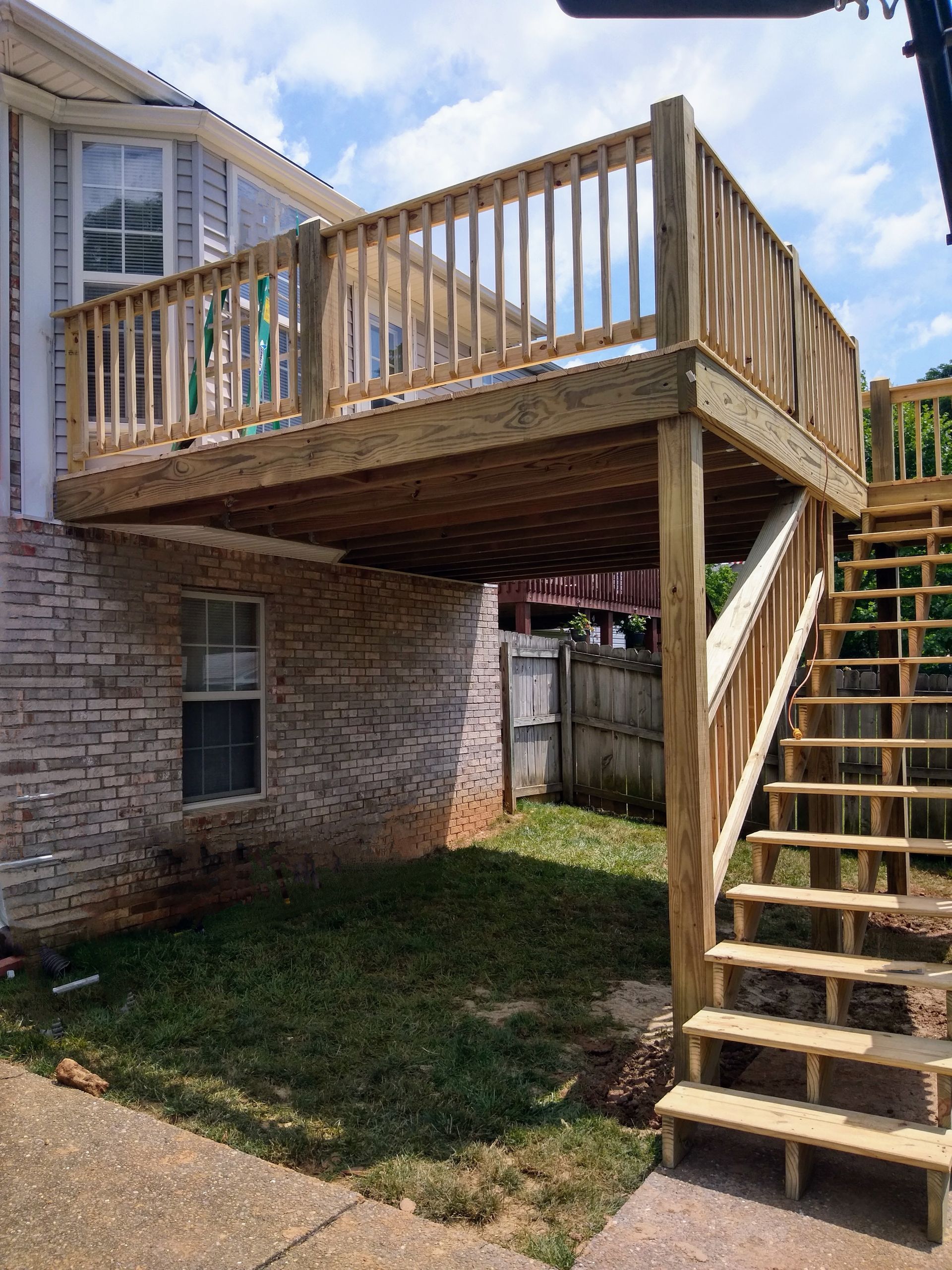 A wooden deck with stairs leading up to it is in the backyard of a house.