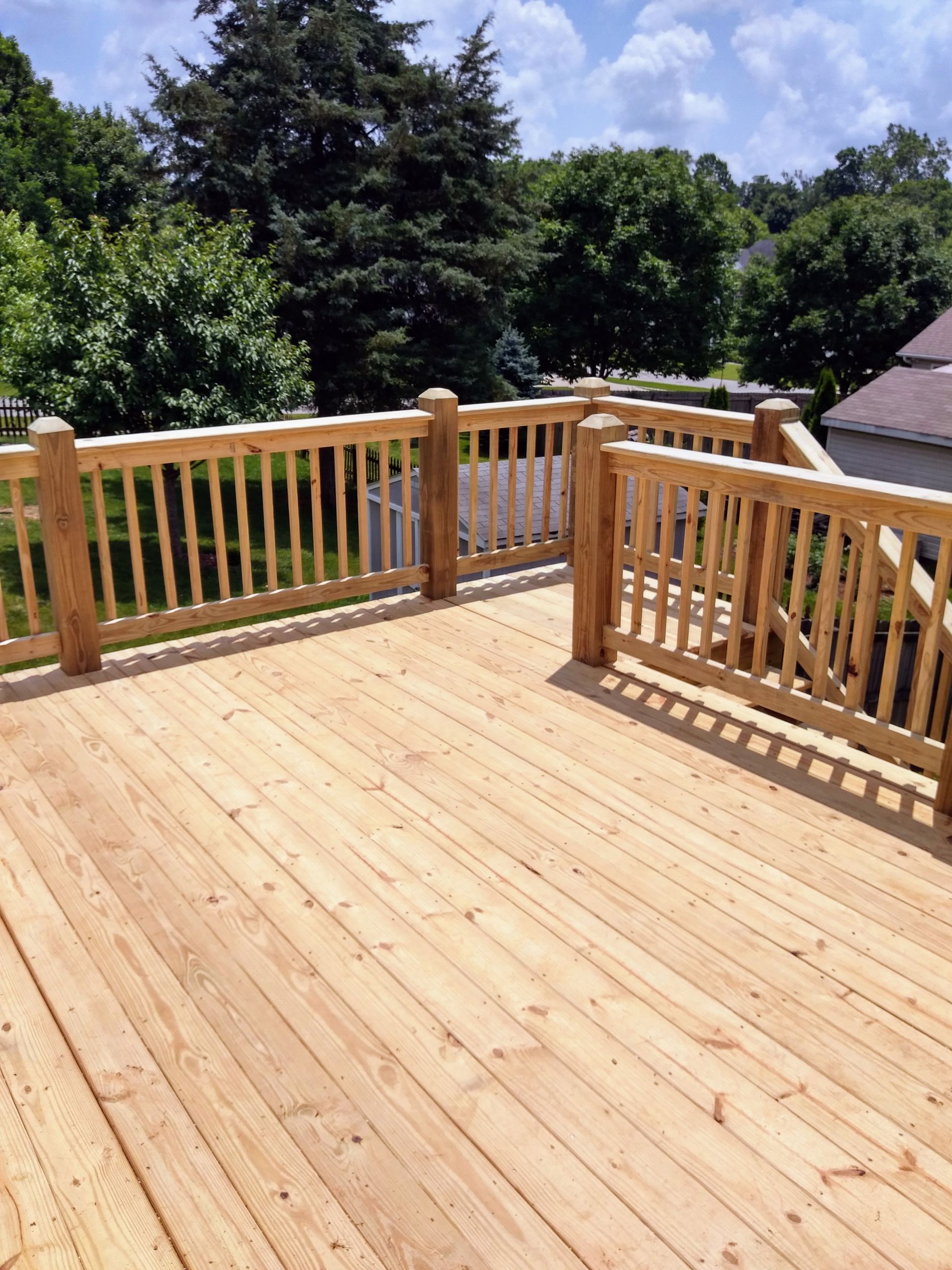 A wooden deck with a wooden railing and trees in the background