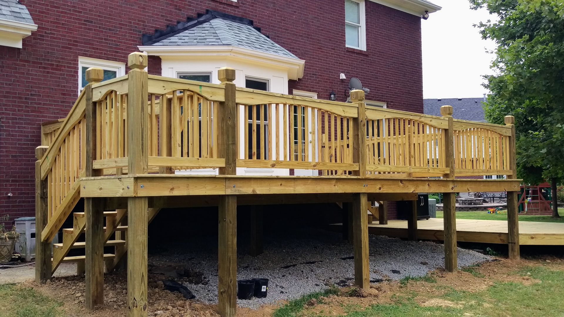 A wooden deck is sitting in front of a brick house.