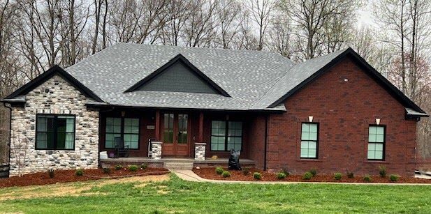 A large brick house with a gray roof is sitting on top of a lush green field.
