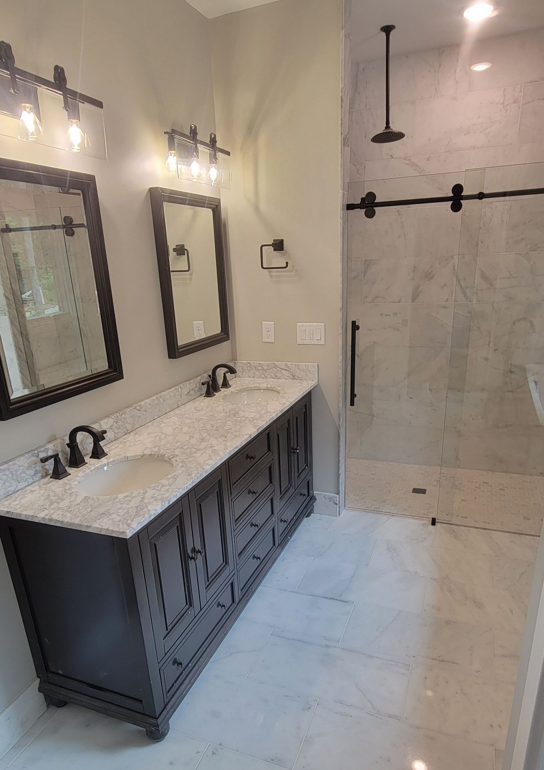 A bathroom with two sinks , two mirrors and a walk in shower.