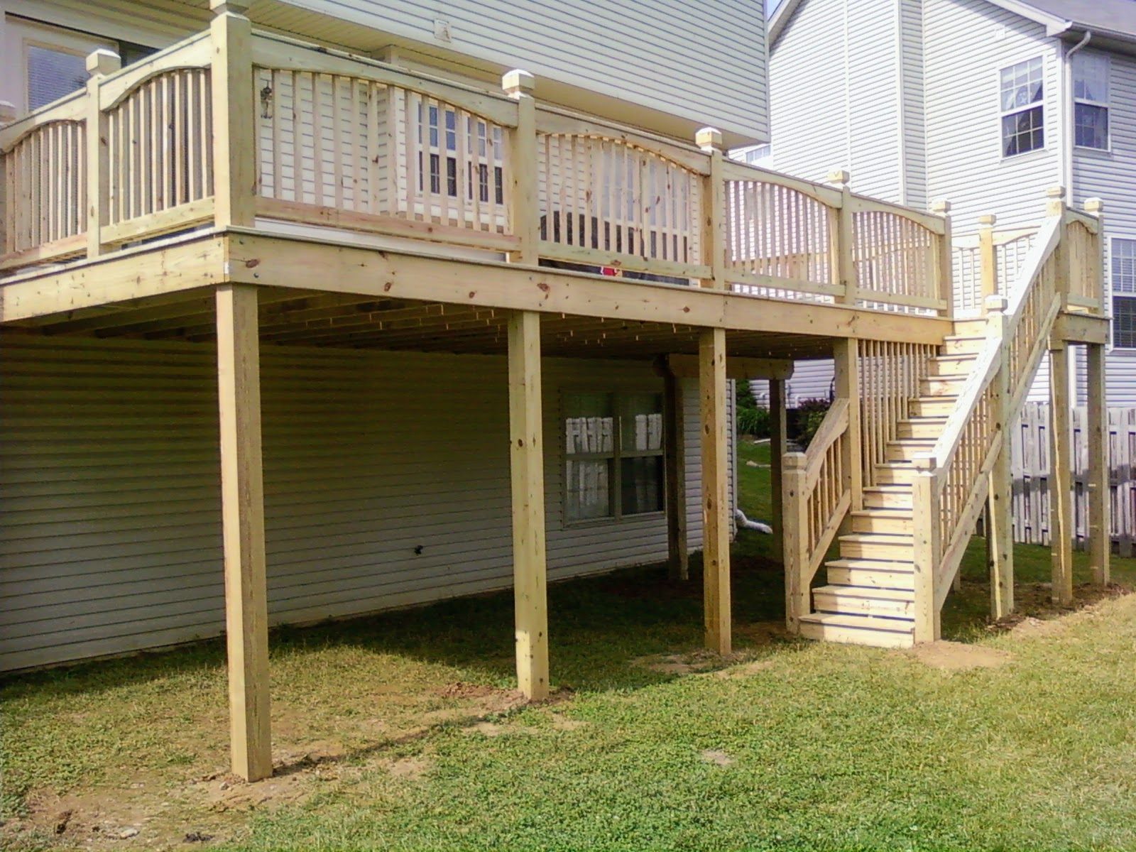 A wooden deck with stairs leading up to it is in the backyard of a house.