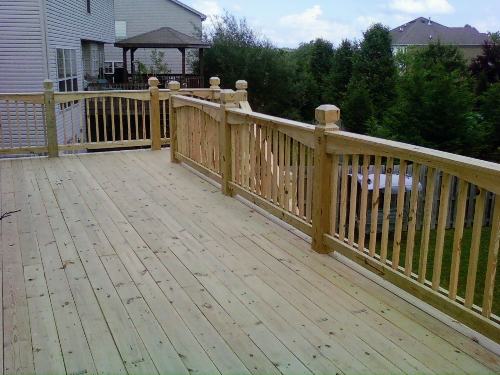 A wooden deck with a wooden railing and a gazebo in the background