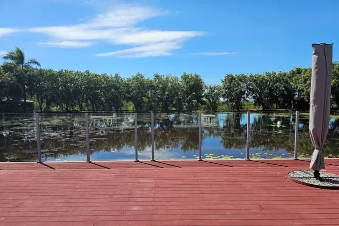 Red Wooden Deck Overlooks a Calm Body of Water and Glass Railing — Villa Lamor in Balberra, QLD