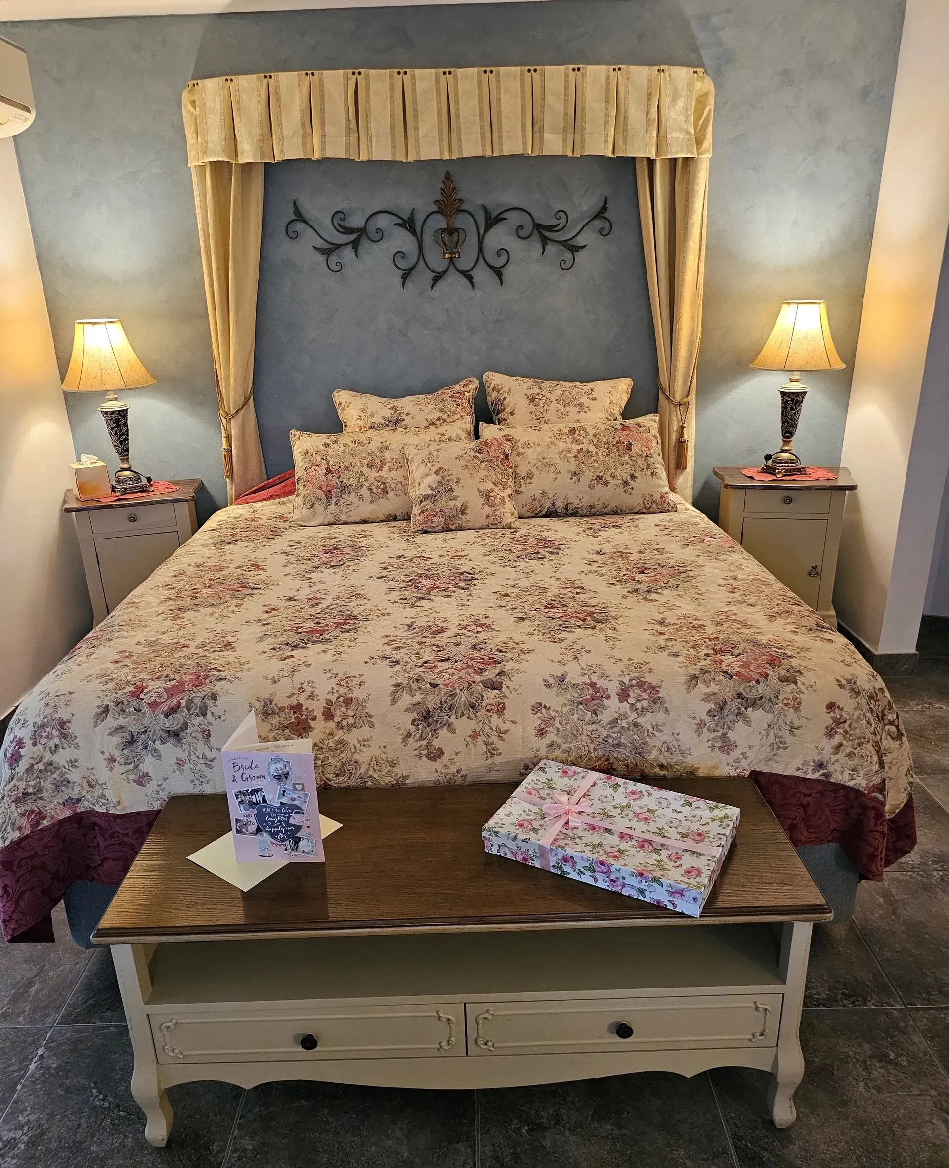 Bedroom With Floral Bedspread, Canopy Bed Frame, Bedside Lamps, and a Wooden Bench — Villa Lamor in Balberra, QLD
