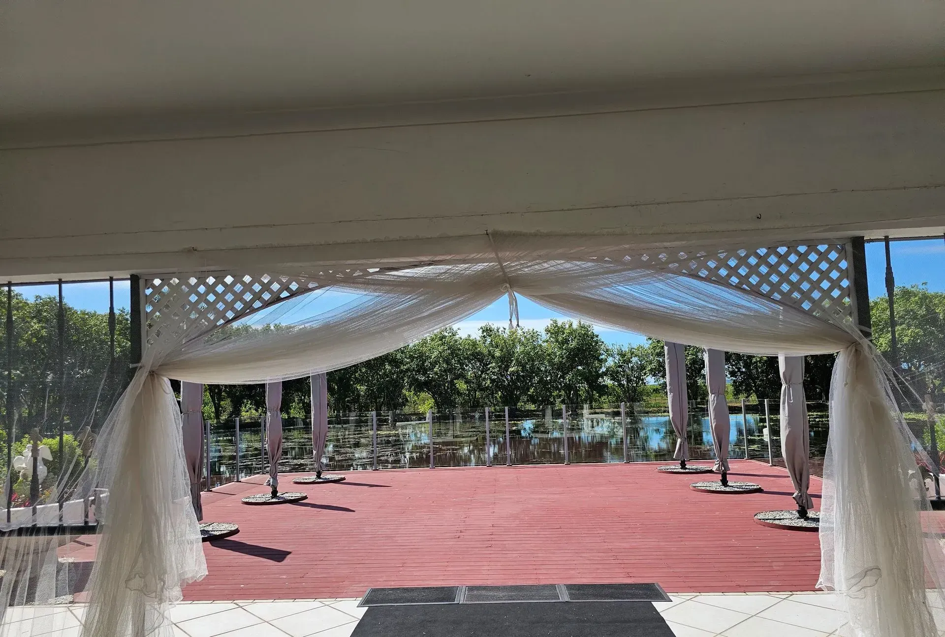 White Fabric Draped Archway With a Red Floor, Overlooking a Waterfront and Trees — Villa Lamor in Balberra, QLD