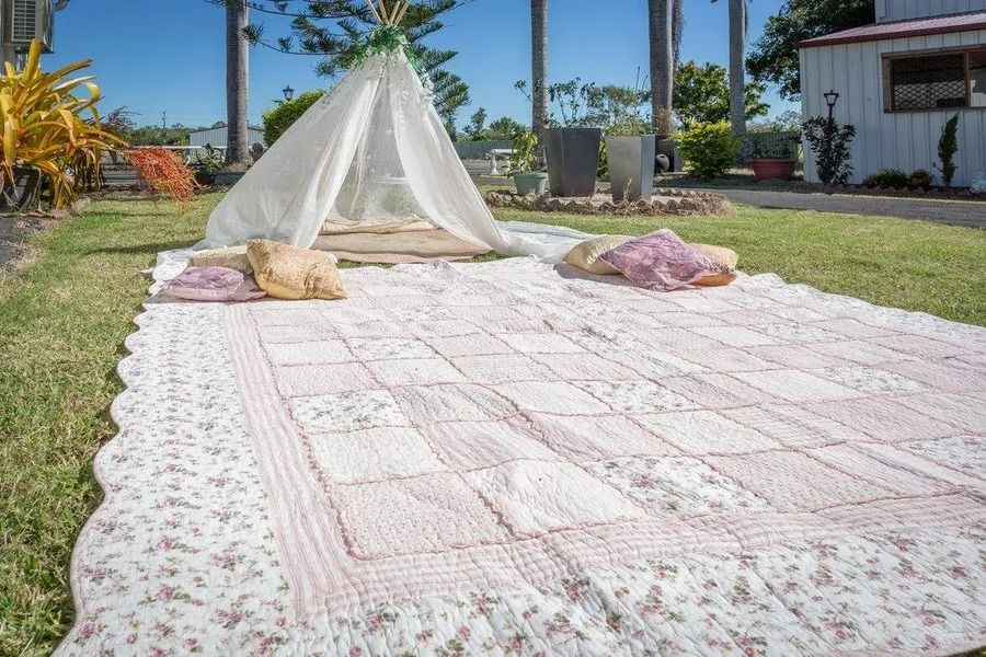 A Picnic Setup on Grass With a White Teepee and Quilt, Featuring Pillows — Villa Lamor in Balberra, QLD