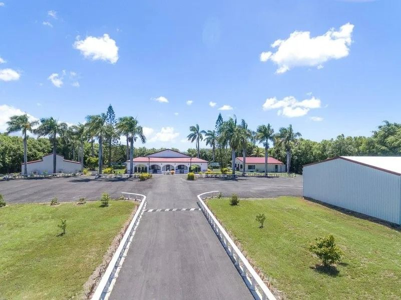Paved Driveway Leads to a Large Building With Palm Trees and a White Wall — Villa Lamor in Balberra, QLD