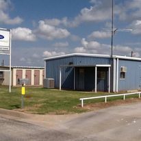 A blue building is sitting on the side of a road next to a grassy field.