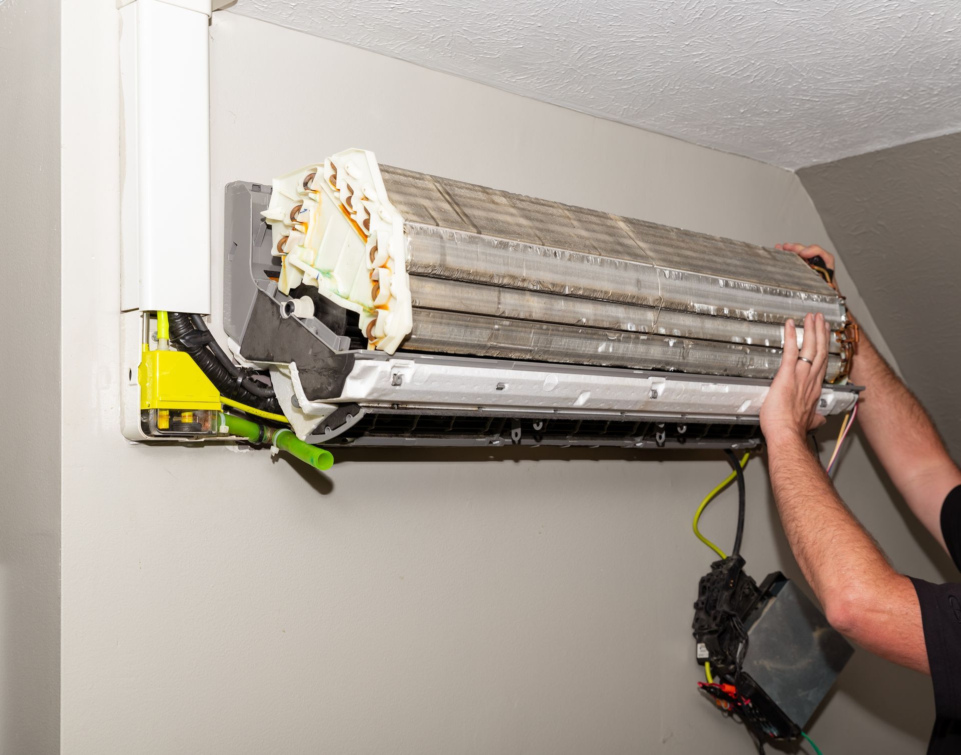 A man is cleaning an air conditioner on a wall.