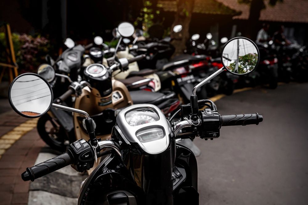 Fila di scooter parcheggiati su una strada asfaltata, in particolare uno nero con dettagli cromati lucidi e specchietti rotondi.