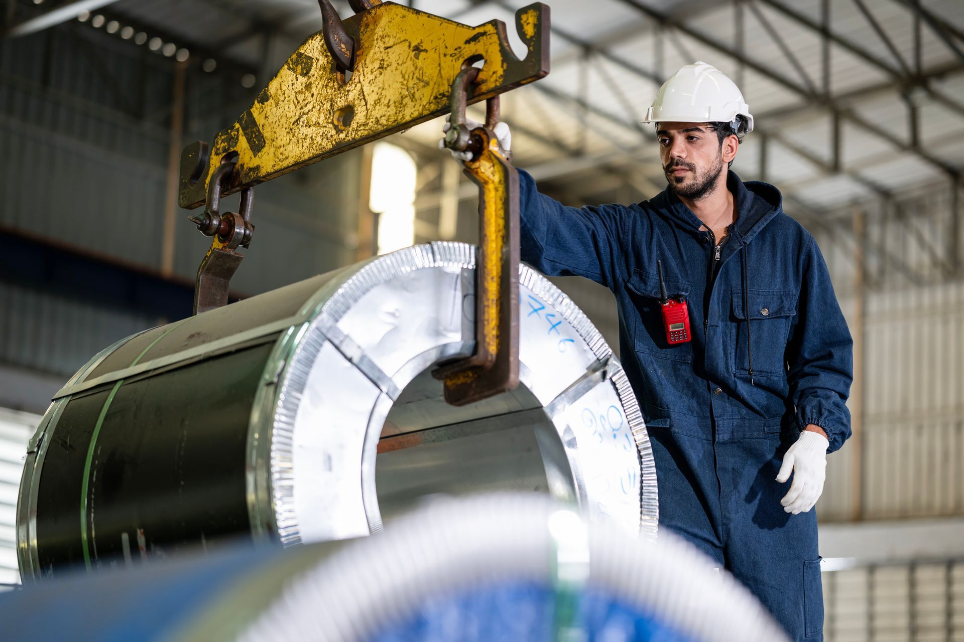 Un uomo solleva un grosso pezzo di metallo con una gru in una fabbrica.