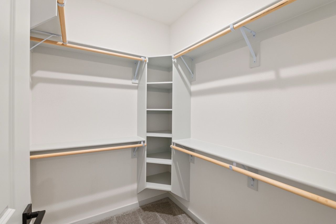 Empty walk-in closet with white built-in shelves and wooden clothing rods.