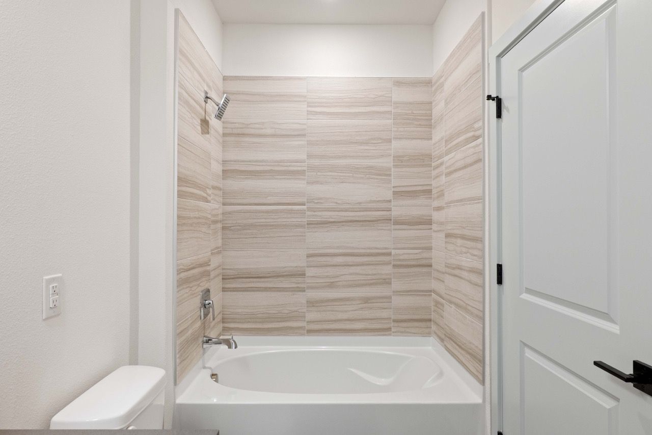 Bathroom with a white tub, beige tile surround, and a toilet.
