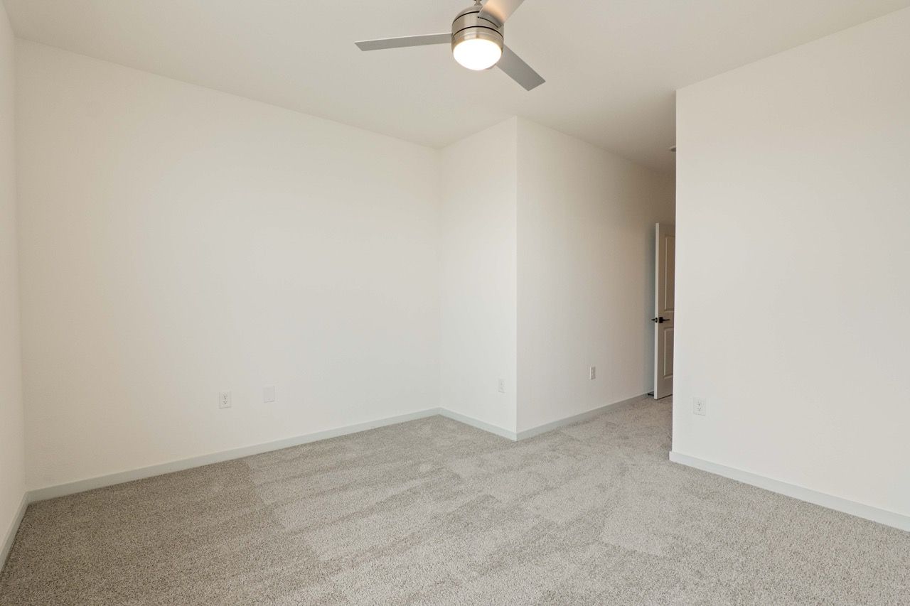 Empty white bedroom with beige carpet, a ceiling fan, and an open doorway.