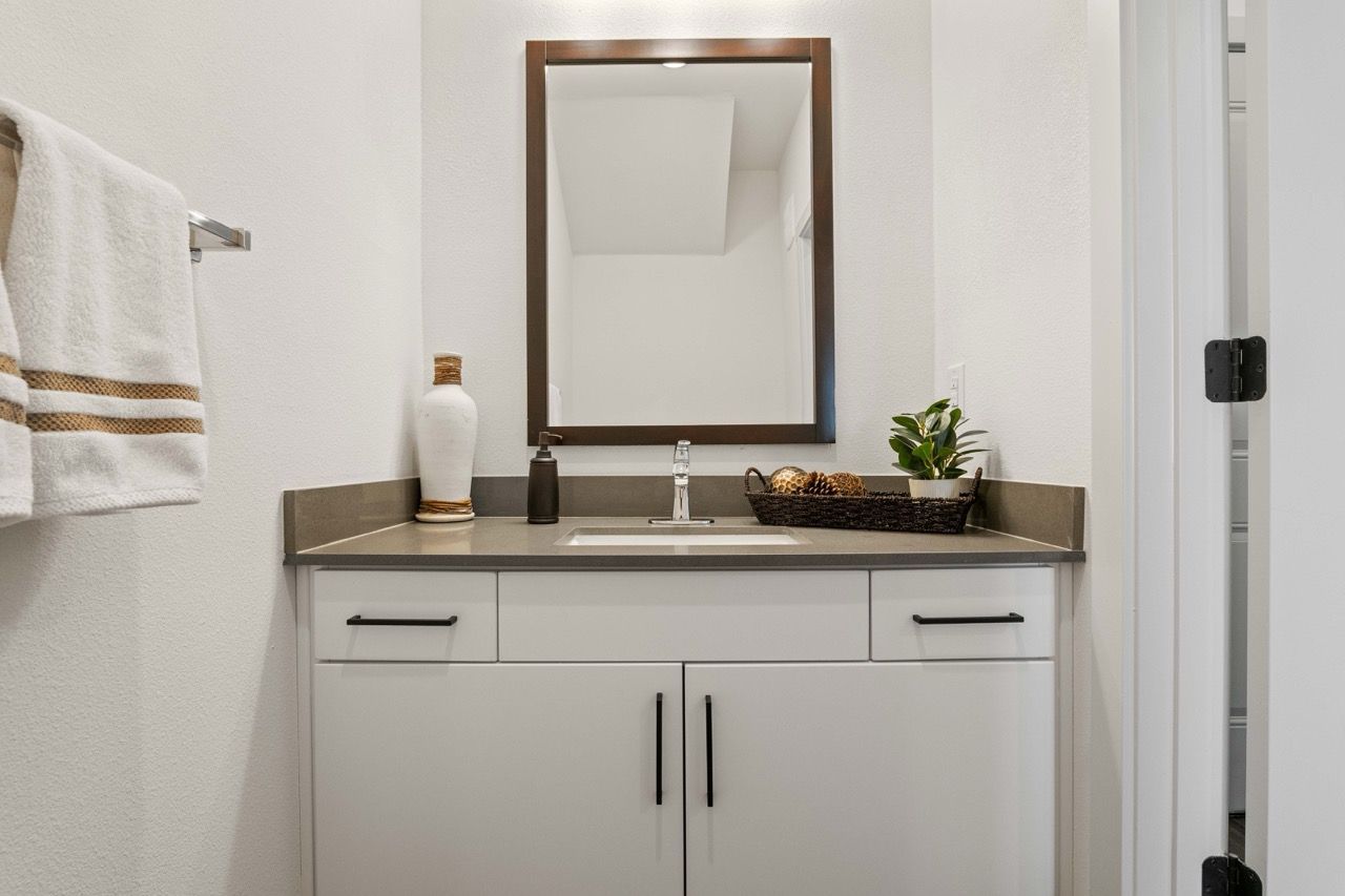 Bathroom vanity with white cabinet, gray countertop, framed mirror, faucet, towel bar, and decorative basket.