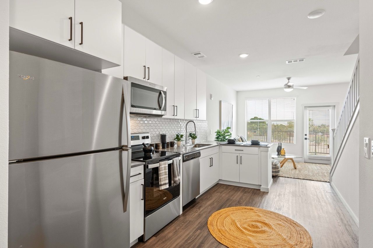 Modern white kitchen with stainless steel refrigerator, microwave, stove, and a round woven rug.