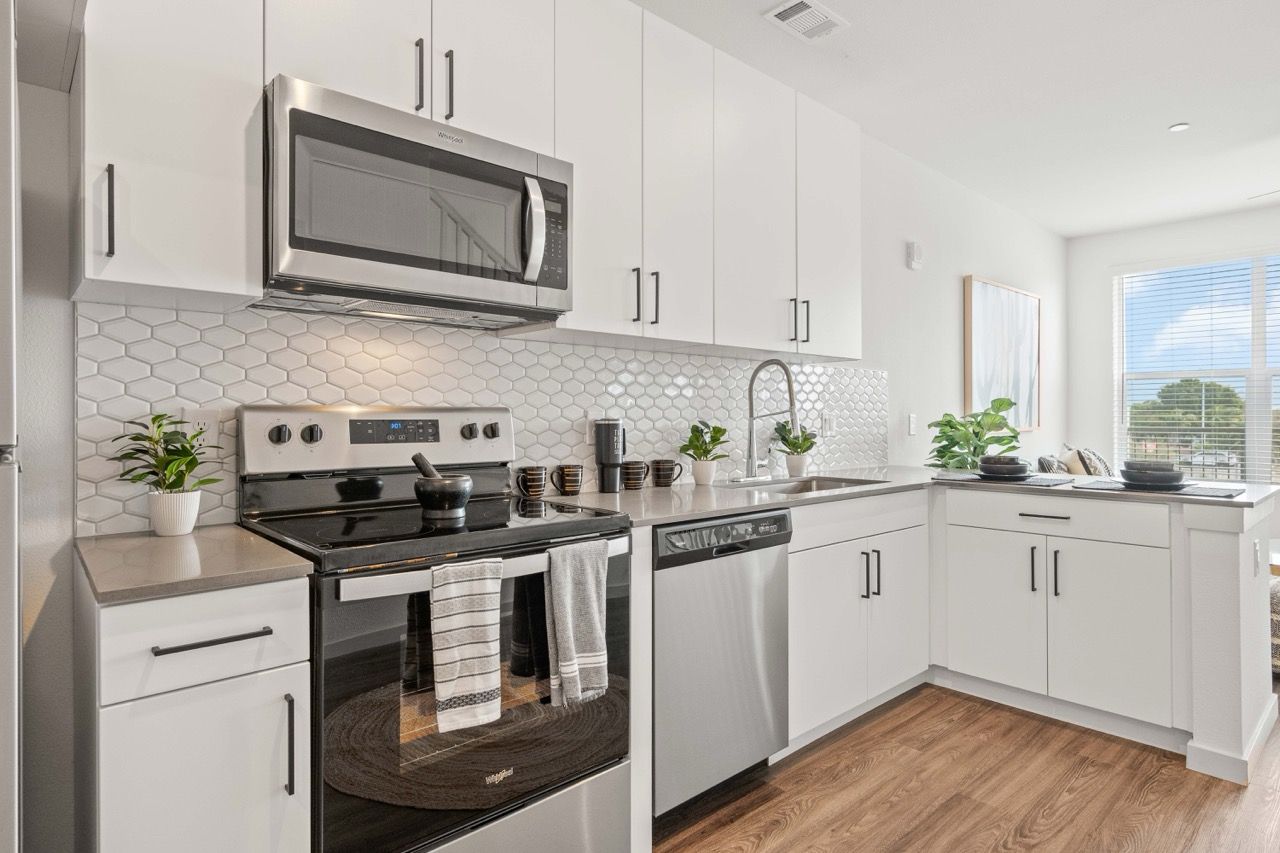 Modern kitchen with white cabinets, stainless steel stove and dishwasher, and a window.