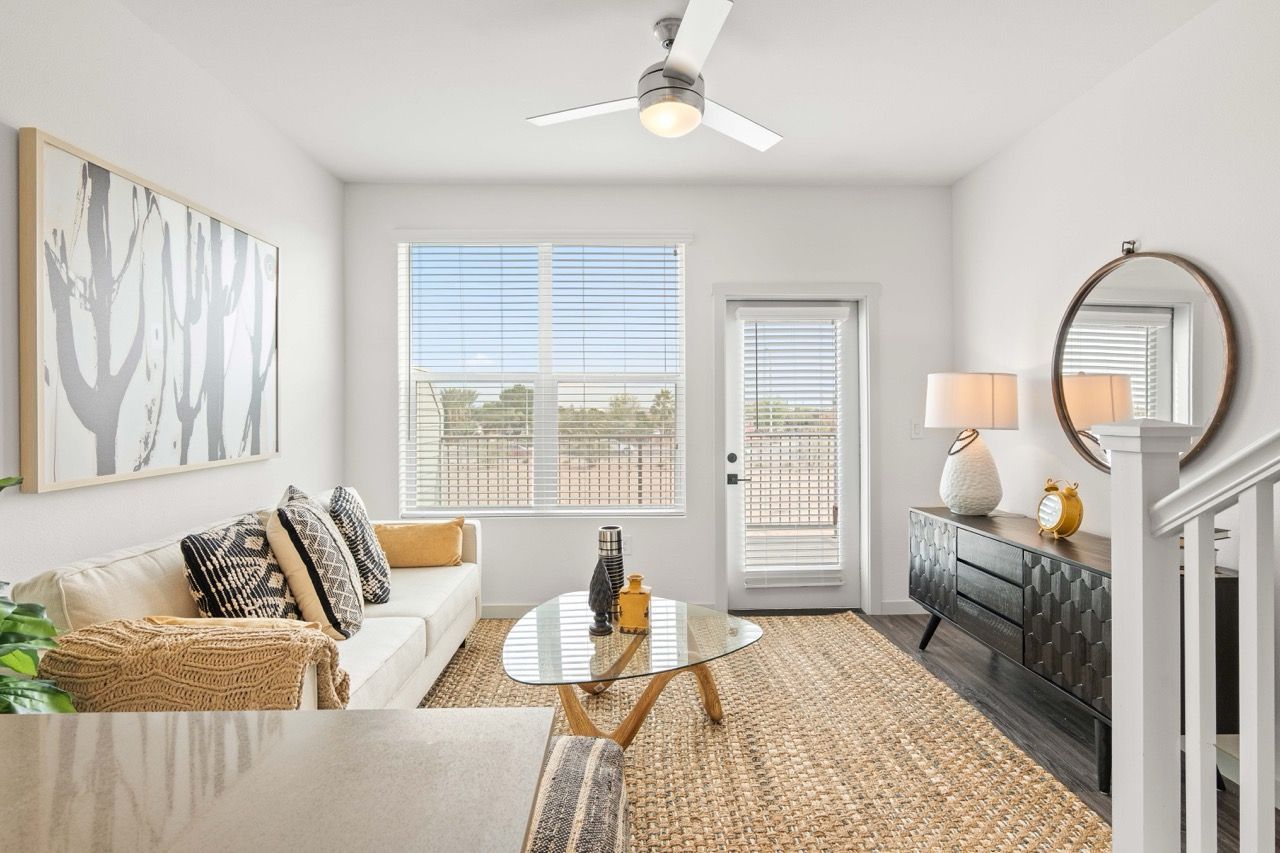 Bright living room in a modern apartment with white walls, beige sofa, glass coffee table, and a round mirror.