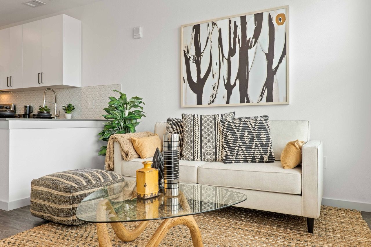 Open-concept living area with a white sofa, glass coffee table, and a nearby kitchen.