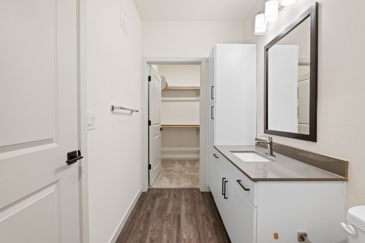 Modern bathroom with white cabinetry, sink and mirror; open walk-in closet visible in background.