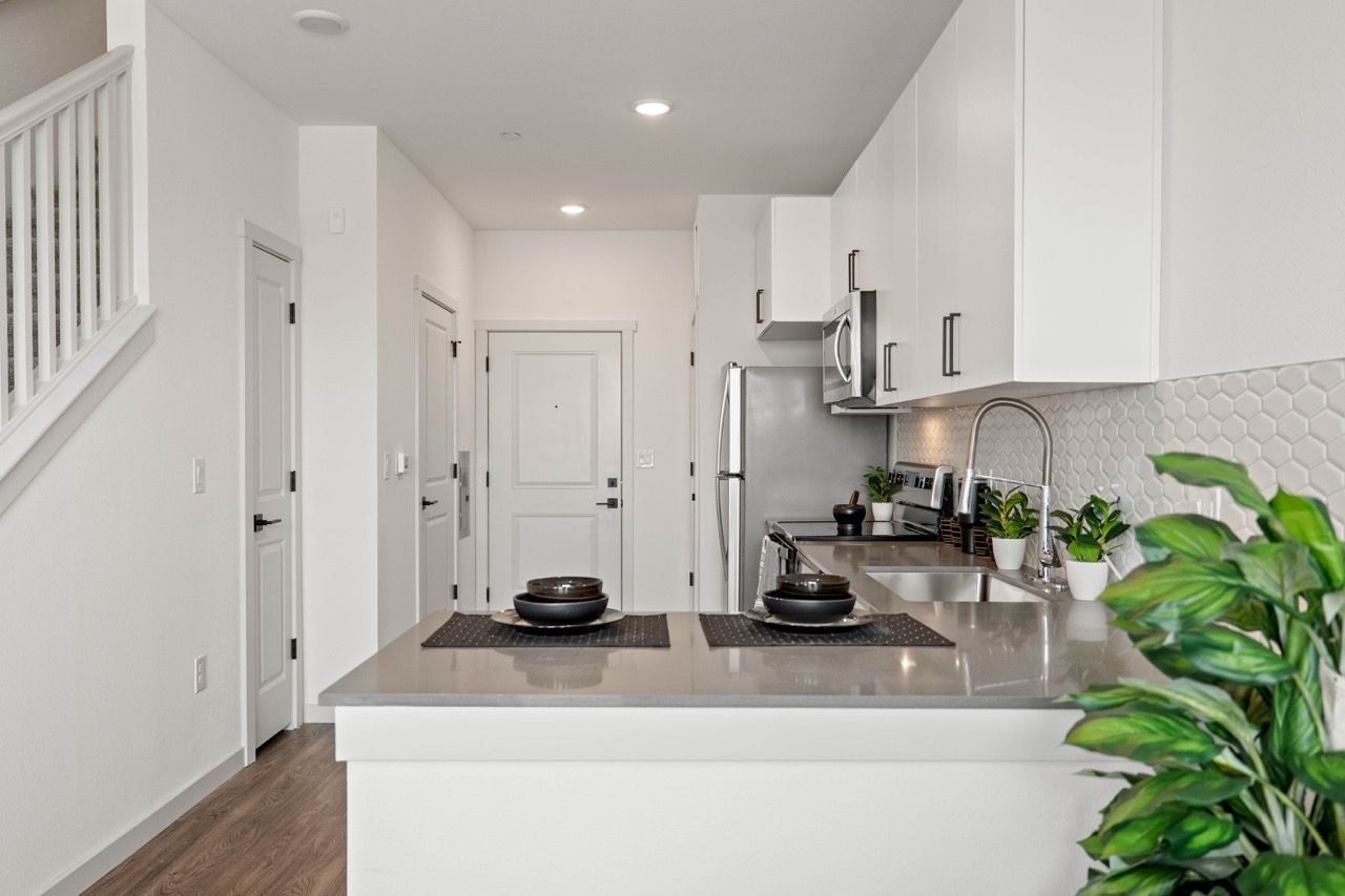 White modern kitchen with island, stainless steel appliances, and potted plants.