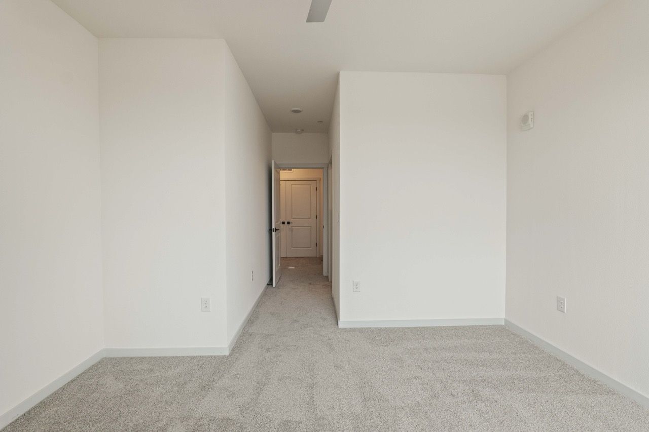 Empty white-walled hallway with light carpet in an apartment, leading to a closed door.