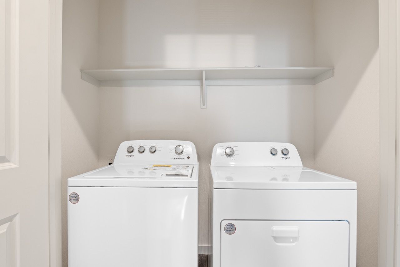 White washer and dryer in a compact laundry closet with a shelf above.