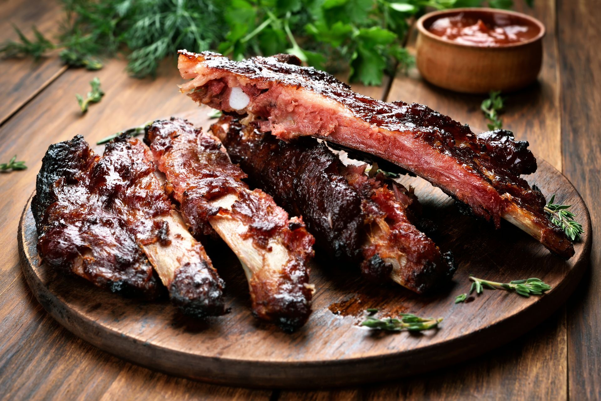 a wooden cutting board topped with ribs and sauce on a wooden table .