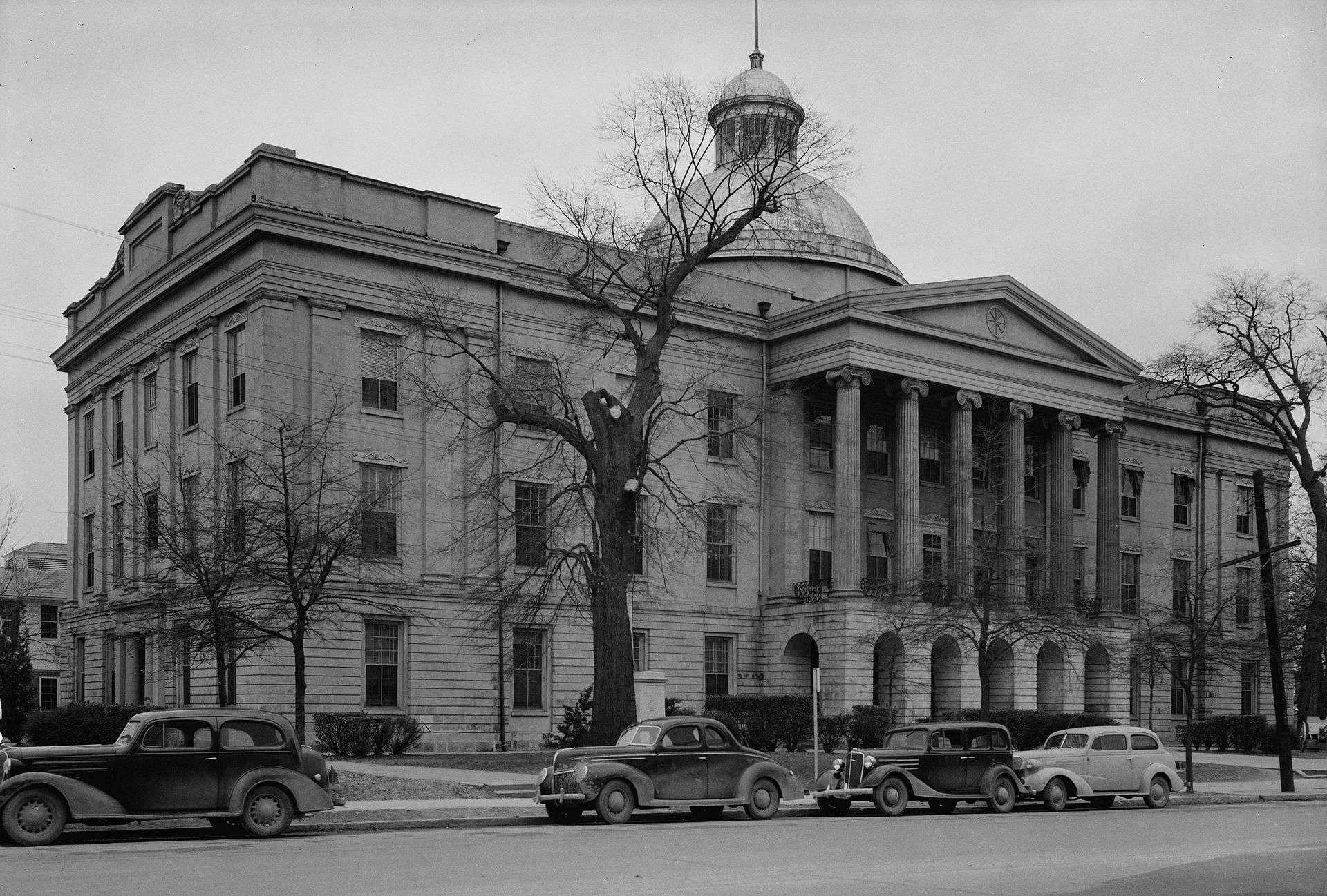 a black and white photo of cars parked in front of a large building