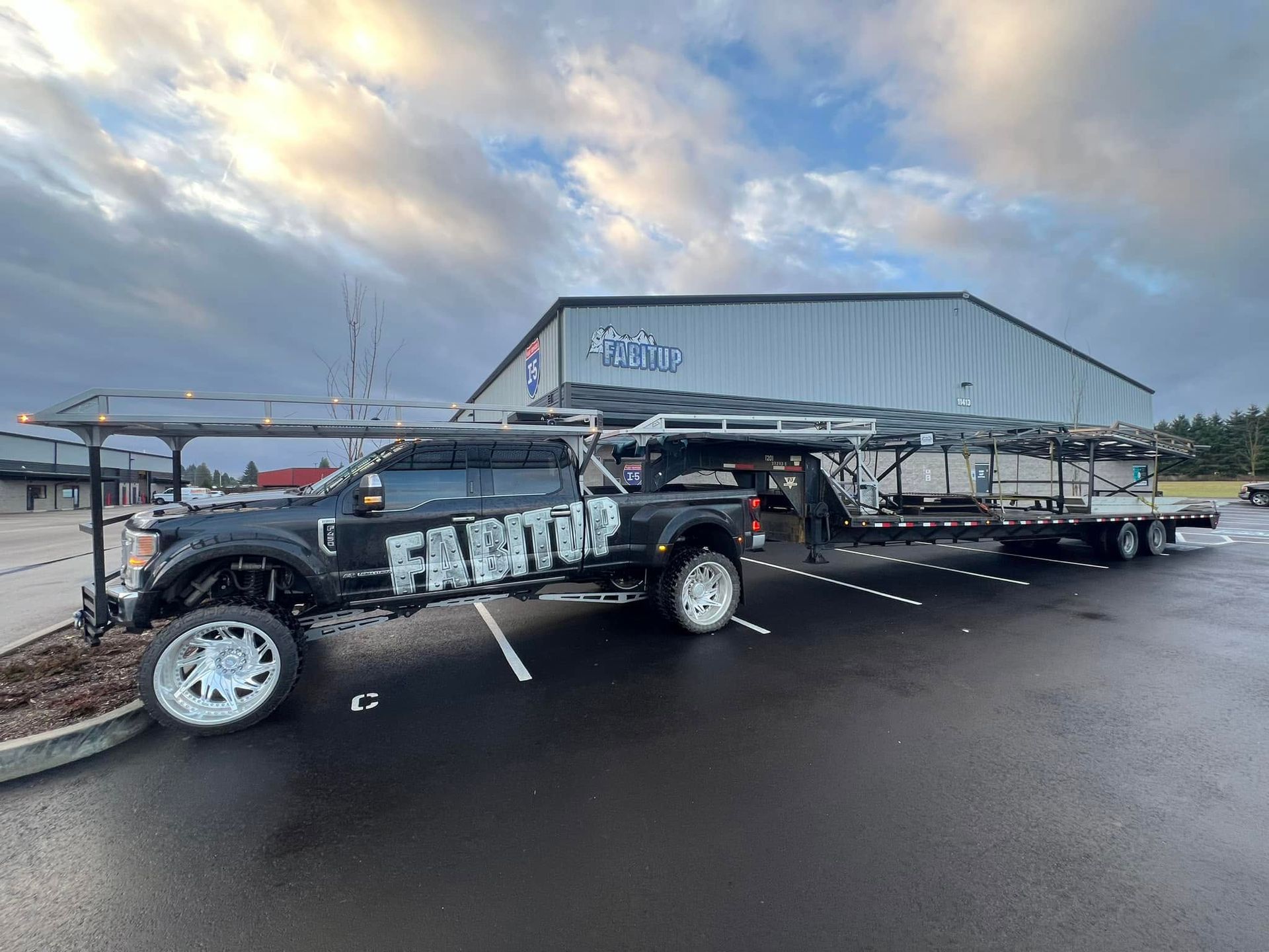 A truck and trailer are parked in a parking lot in front of a building.