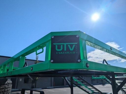 A green utv trailer is parked in front of a building.