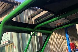 A green vehicle with a sunroof is parked in front of a building.