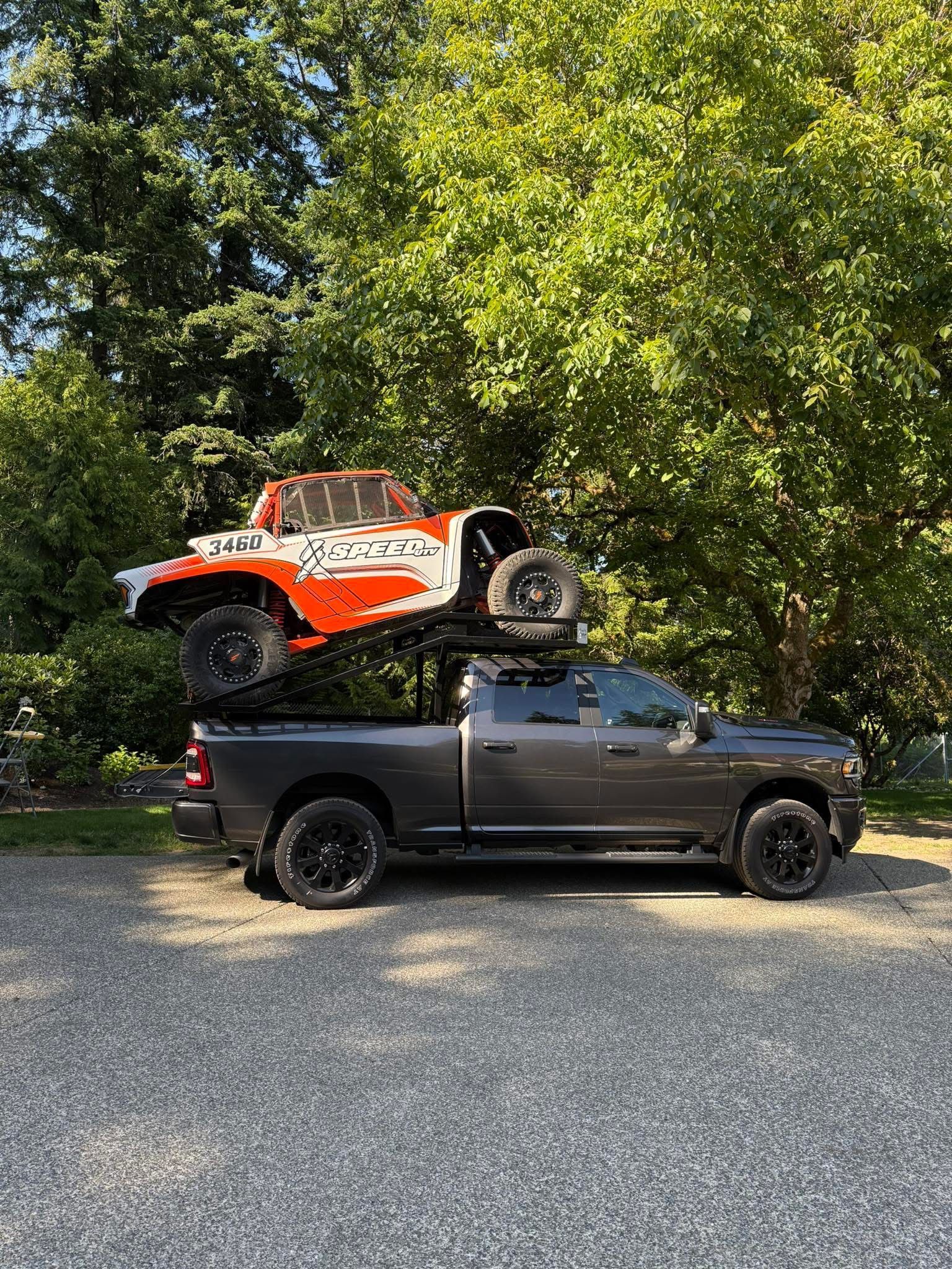 A truck with a polaris rzr on top of it is parked in a gravel lot.