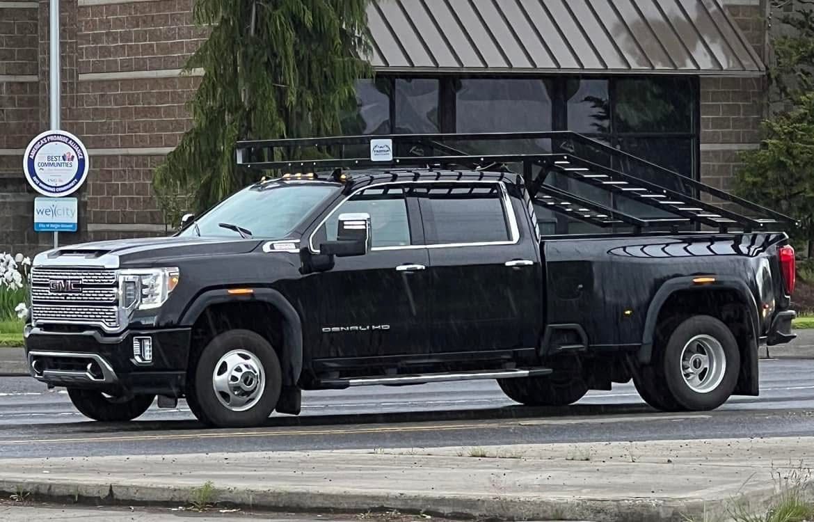 A black truck with a roof rack on top of it is parked in front of a building.