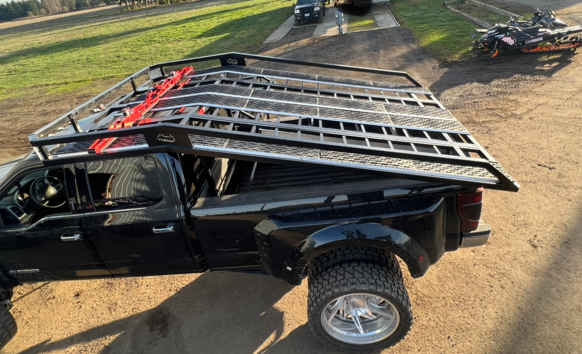A black truck with a roof rack on top of it is parked on a dirt road.